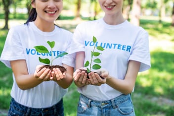 Two volunteers holding green plants to add to a community garden
