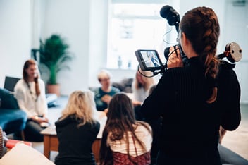 Skilled volunteer holding a camera, filming others sitting around a table. 