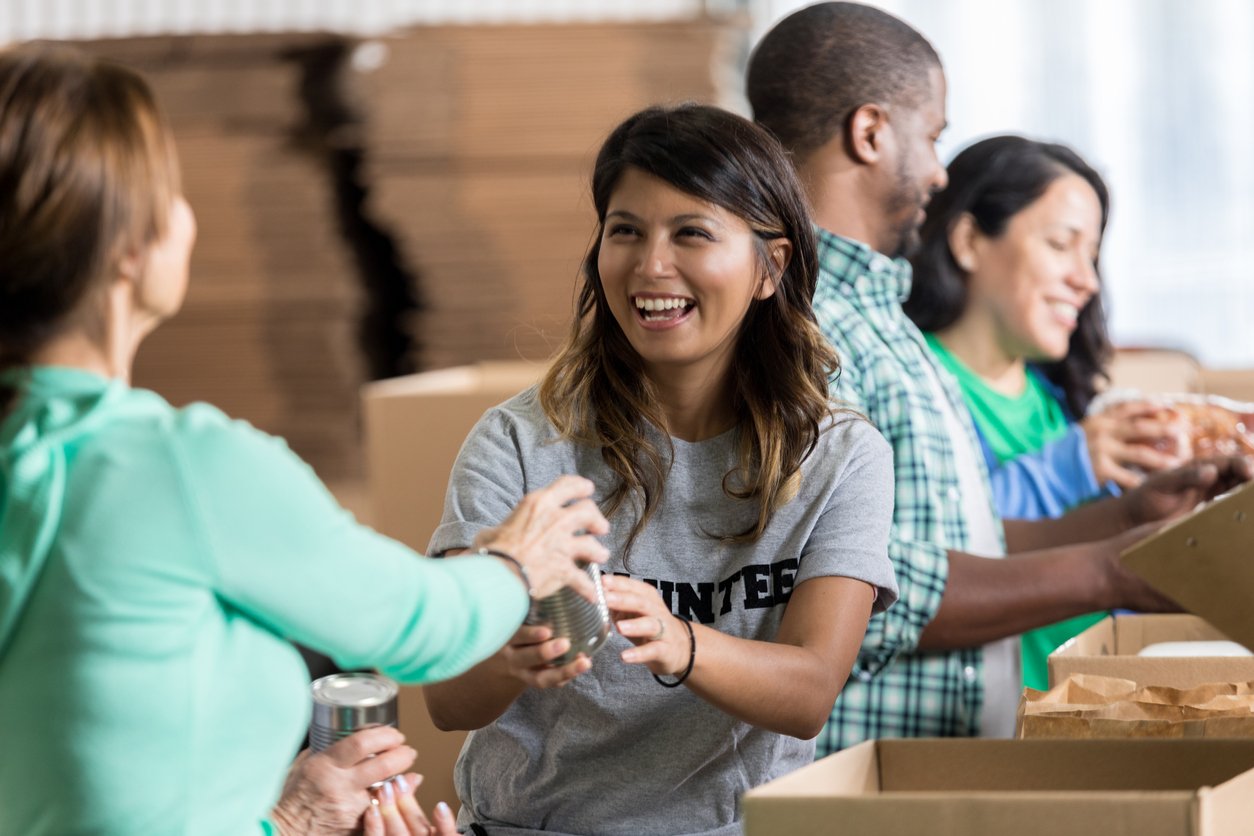 Cheerful mid adult Hispanic female volunteer accepts a canned food donation during a community food drive.